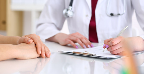 Unknown doctor woman consulting patient while filling up an application form at the desk in hospital. Just hands close-up. Medicine and health care concept