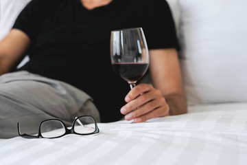 Young handsome businessman relaxing on bed in hotel room with a glass of wine after a tough day at work