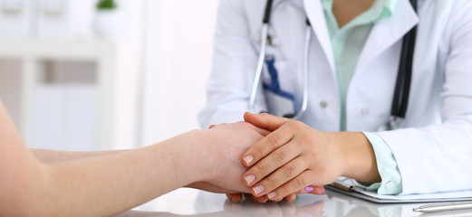 Hand of a doctor woman reassuring to female patient, close-up. Medical ethics and trust concept
