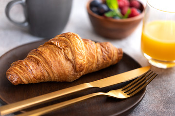 Close up of fresh baked croissant on wooden plate with gold cutlery. Typical ingredient for breakfast in cafe or restaurant.