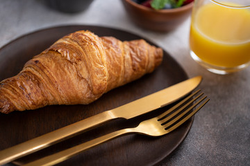 Close up of fresh baked croissant on wooden plate with gold cutlery. Typical ingredient for breakfast in cafe or restaurant.