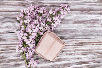 Lilac flowers and small gift box from paper with surprise on wooden background. Greeting card. Spring gift. Top view. Flat lay.