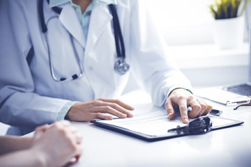 Fototapeta premium Doctor and female patient sitting at the desk and talking in clinic near window. Medicine and health care concept. Green is main color