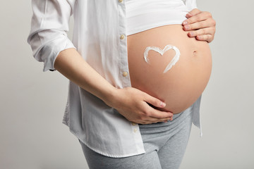 Studio shot of happy pregnant woman dressed in comfort home suit touching gently her belly and smiling at camera