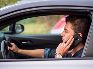 Attractive young man sitting in his car talking on cell phone, while driving