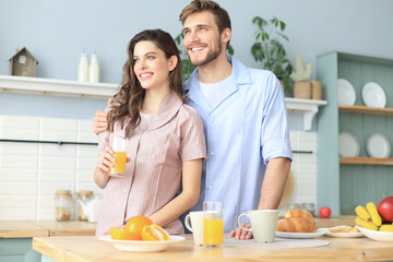 Obraz na płótnie Canvas Portrait of happy young couple in pajamas cooking together in the kitchen, drinking orange juice in the morning at home.