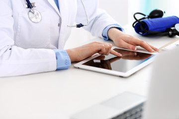 Doctor working table. Woman physician using tablet computer while sitting in hospital office close-up. Healthcare, insurance and medicine concept