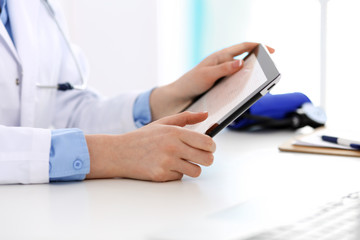 Doctor working table. Woman physician using tablet computer while sitting in hospital office close-up. Healthcare, insurance and medicine concept