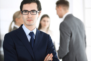 Headshot of businessman standing straight with colleagues at background in office. Group of business people discussing questions at conference or presentation. Success and business concept