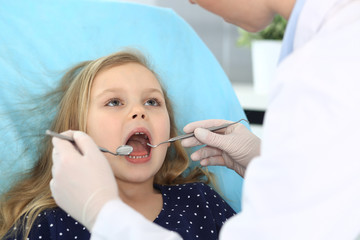 Little baby girl sitting at dental chair with open mouth and feeling fear during oral check up while doctor. Visiting dentist office. Medicine concept