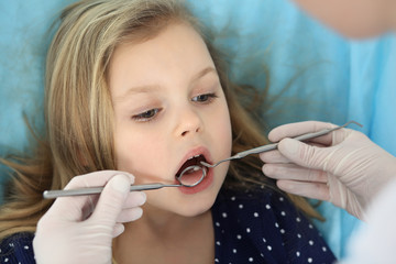 Little baby girl sitting at dental chair with open mouth and feeling fear during oral check up while doctor. Visiting dentist office. Medicine concept