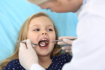 Little baby girl sitting at dental chair with open mouth during oral check up while doctor. Visiting dentist office. Medicine concept