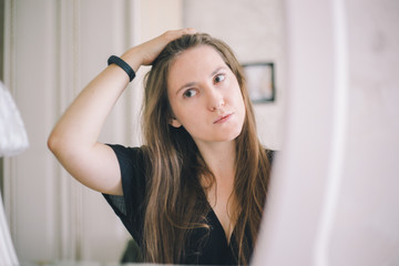Close-up of a girl of European appearance straightens hair in a mirror in a bright hotel room