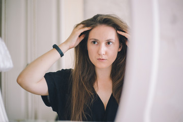 Fototapeta premium Close-up of a girl of European appearance straightens hair in a mirror in a bright hotel room
