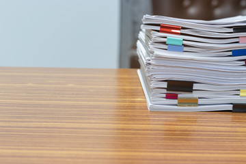 Close up pile of unfinished paperwork on office desk waiting to be managed and inspected. Stack of homework assignment with colorful paper clips. Report papers stacks. Business and education concept.