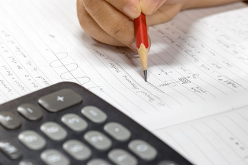 Close-up hand holding red pencil for compute the Physics problem using Mathematics knowledge and calculator. Concept of Education and Troubleshooting.