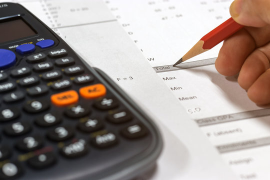 Hand holding pencil and calculator on paper of final grade for each course at the end of semester. The number of grade points a student earned in a given period of time. Grading in education concept.