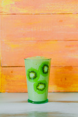 Green smoothie of celery and banana in glass decorated with slices of kiwi on wooden orange background. Healthy vegan lifestyle
