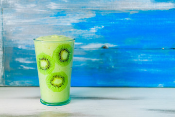 Green smoothie of celery and banana in glass decorated with slices of kiwi on wooden blue background. Healthy vegan lifestyle