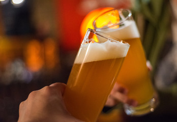 Close-up view of a two glass of beer in hand. Beer glasses clinking in bar or pub