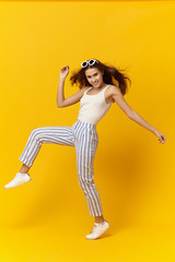 Fototapeta na wymiar Joy, happiness, fun and good mood concept. Full length image of adorable vibrant young female with long loose hair dancing at yellow blank studio wall with copyspace for your advertising content