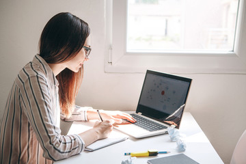 A young beautiful student girl does homework or writes a to-do list or this girl works in a home office. Home education or business or planning.