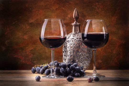Still life with wine, a glass bottle in a metal braid, and a vine, on a textured background, and a wooden table top