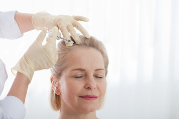 Naklejka premium Middle aged woman gets cosmetic injection in her forehead. Hyaluronic acid injection for facial rejuvenation procedure. Woman in beauty salon. Plastic surgery clinic.