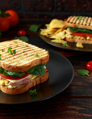 Sandwich with ham, cheese, tomatoes, spinach, corn, mayonnaise, mustard, gherkins, toasted bread and potato chips.