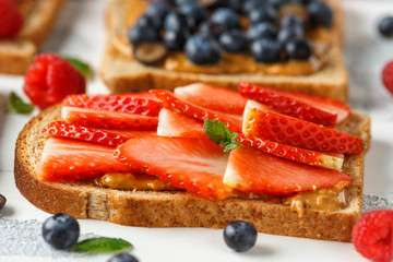 Peanut butter sandwiches with fresh strawberry, blueberry, raspberry and banana whole meal toasts.