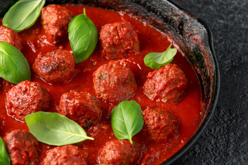 Homemade Meatballs in iron cast with sweet and hot tomato sauce, basil. On wooden table