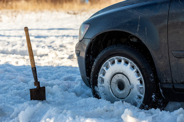 car stuck in snow offroad at daylight with shovel and selective focus