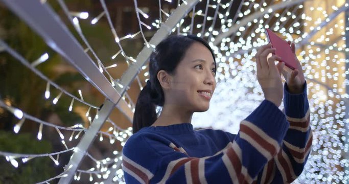 Woman take photo on cellphone with beautiful christmas light decoration at night