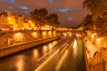 Fototapeta na wymiar Evening cruise on Seine river in slow motion and people hanging out along embankment of Ile de la Cite at night time in Paris downtown, France