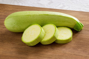 One fresh green courgettes and few slices on a brown wooden cutting board. Cook at home. Fresh farm vegetables and healthy vegetarian food.