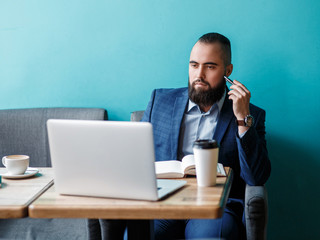 Businessman bearded man in a suit works behind the laptop sitting in a comfortable office coworking.
