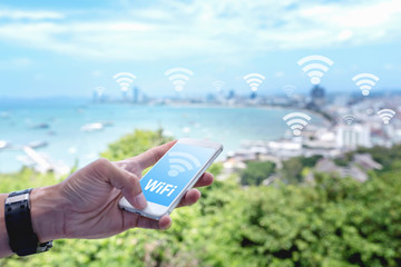 Close up of hand using mobile phone with free WiFi icon on blurred city background. Free WiFi internet concept.