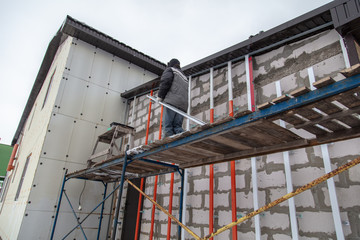 A worker installs a metal profile on the walls of a siding house