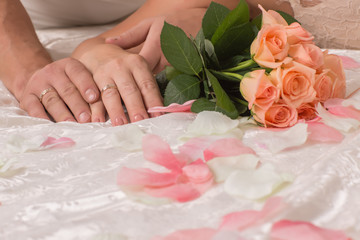 Hands bride and groom holding a beautiful colorful blooming bouquet of roses, lie on the bed
