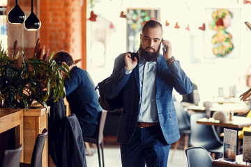 Young bearded businessman walks into a stylish loft office talking on the phone.