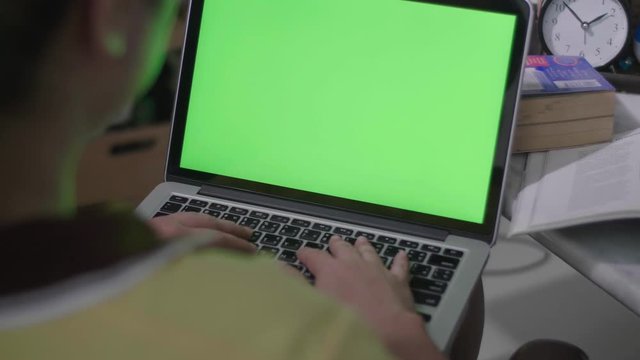 Woman working on the laptop computer with green screen at home. Chroma key. View from the back. 