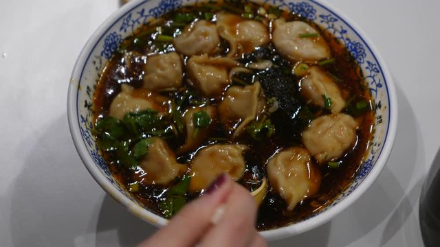 Damplings soup in bowl, woman hand with spoon stir hot food