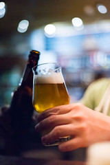 man's hand holds a bottle and glass of beer in bar
