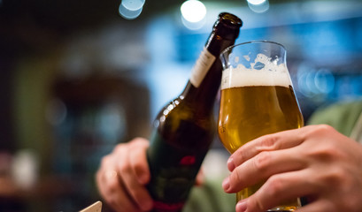 man's hand holds a bottle and glass of beer in bar