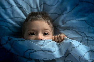 boy in bed with his eyes open. the child is afraid of the dark. tormented by nightmares and terrible dreams in children