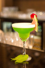 Green alcoholic cocktail with mint in a margarita glass on a bar counter