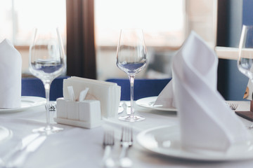 Close-up table in a restaurant. Glasses for wine, forks, spoons, napkins on a blurred light background