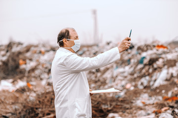 Side view of Caucasian ecologist in white uniform estimating pollution on landfill.