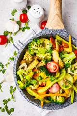 Fried broccoli, peppers, corn, zucchini and tomatoes in pan on a white background.