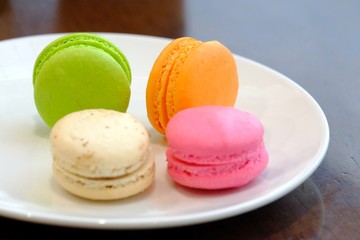 In senlective focus a group of macaroons,famous French dessert in a white plate with wooden dinning table 